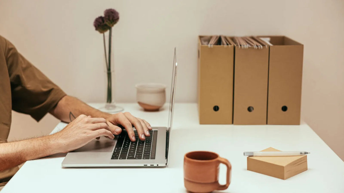 Persona escribiendo en una laptop en un espacio de trabajo sencillo