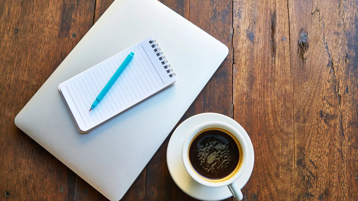 Libreta, bolígrafo y una taza de café sobre una laptop cerrada
