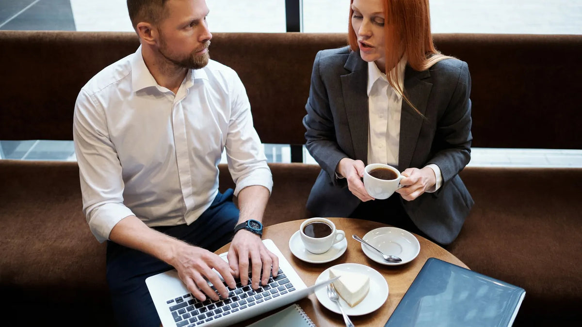 Dos profesionales conversando en una mesa de reunión con una laptop