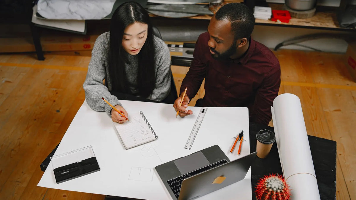 Dos personas planificando sobre una mesa con hojas y una laptop