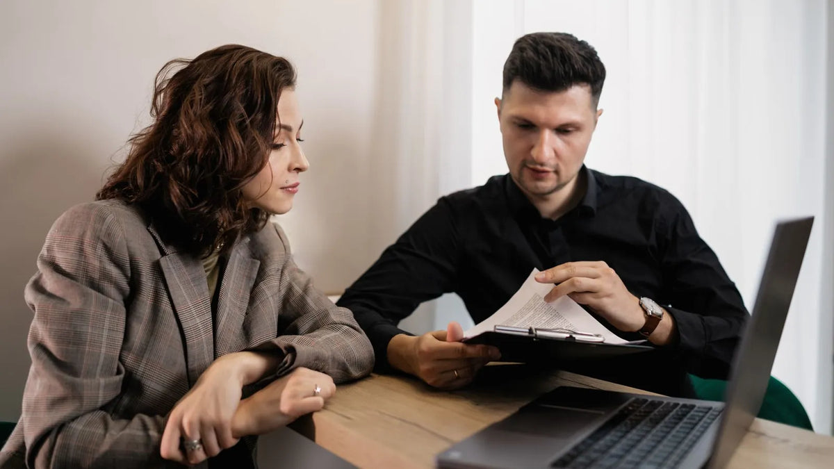 Dos personas revisando un documento junto a una laptop