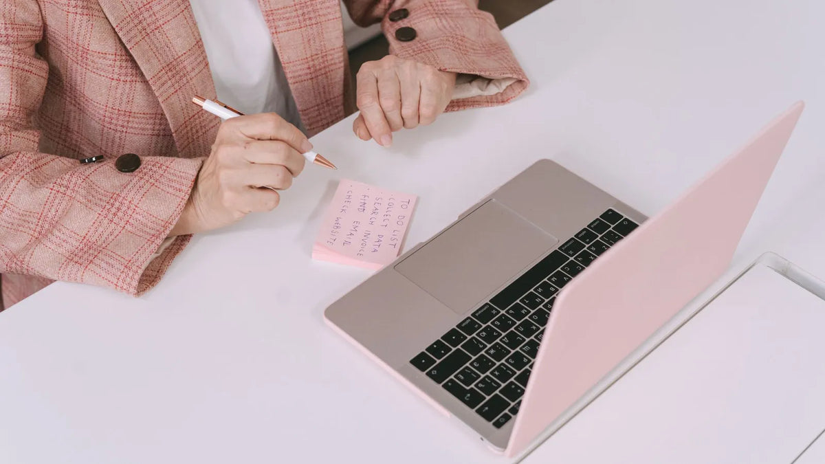 Persona tomando notas en un cuaderno junto a su laptop