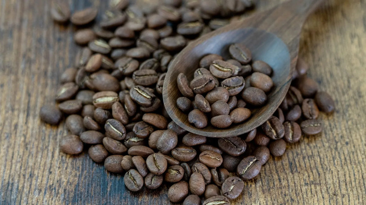 Granos de café tostado y una cuchara de madera sobre una mesa