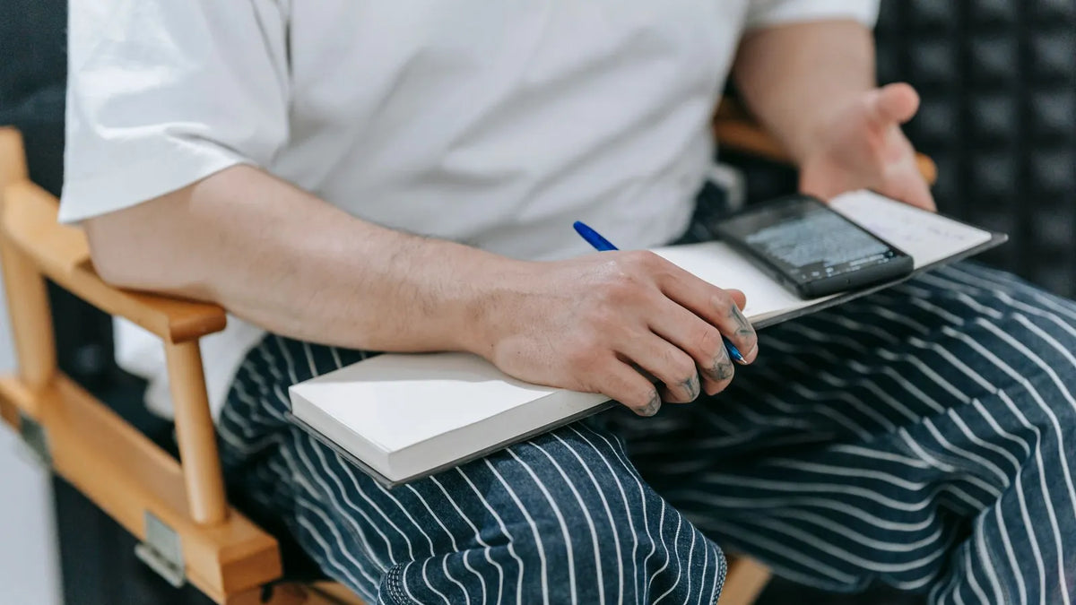 Persona escribiendo un guion en un cuaderno junto a un teléfono sobre el escritorio