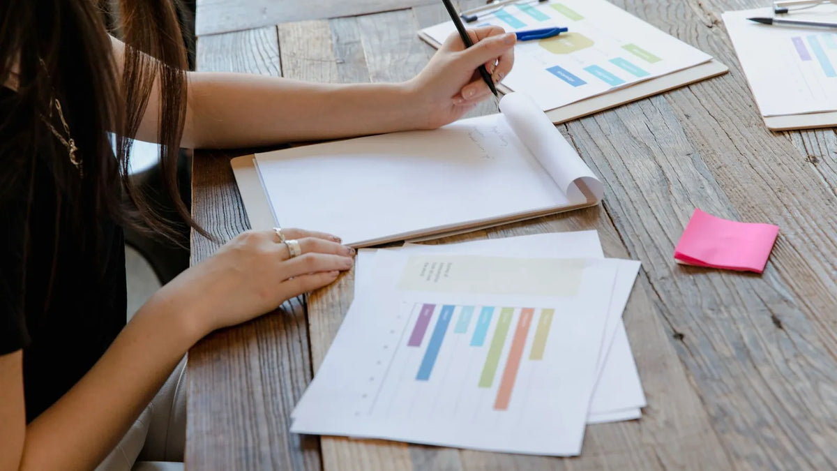 Persona revisando gráficos impresos y notas sobre una mesa