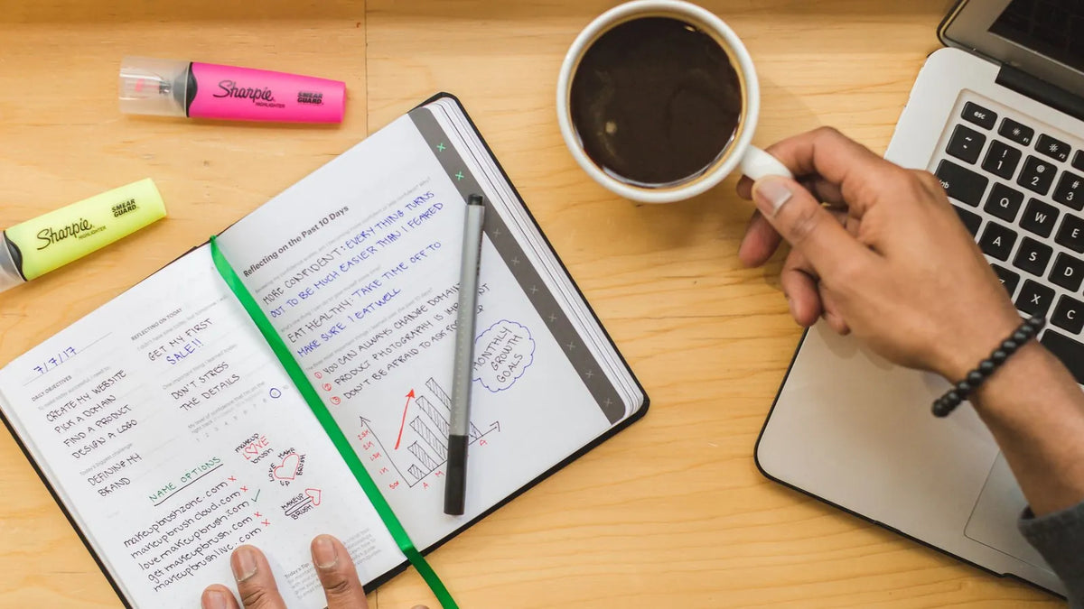 Cuaderno con notas, una taza de café y una laptop sobre un escritorio
