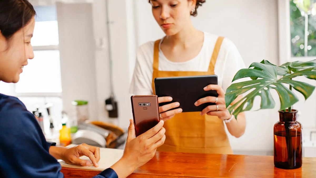 Dueña de un negocio atendiendo a una clienta con una tablet en el mostrador