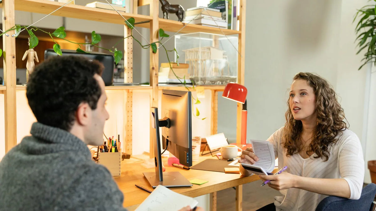 Dos personas conversando en una reunión de trabajo en una oficina pequeña