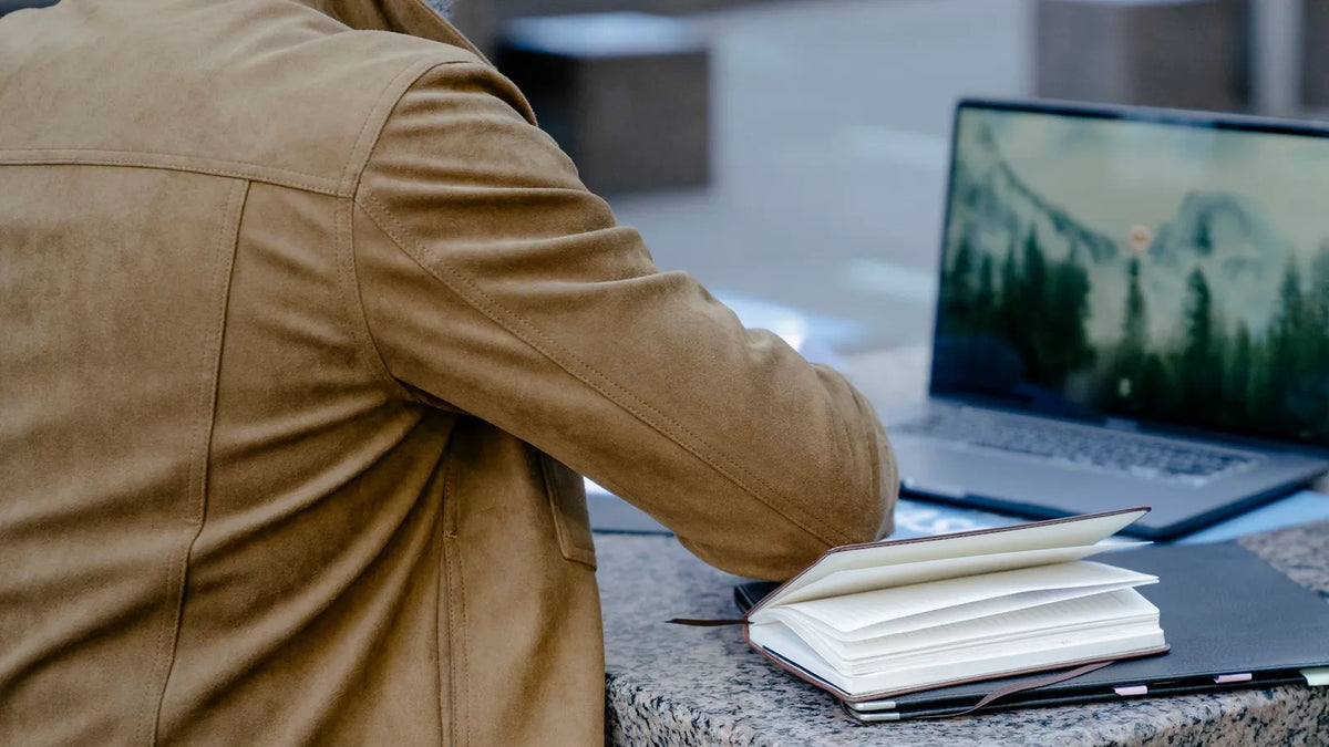 Persona planificando su semana de trabajo en un cuaderno junto a una laptop