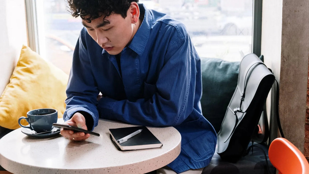 Persona leyendo la pantalla de un teléfono con gesto pensativo en la mesa de un café