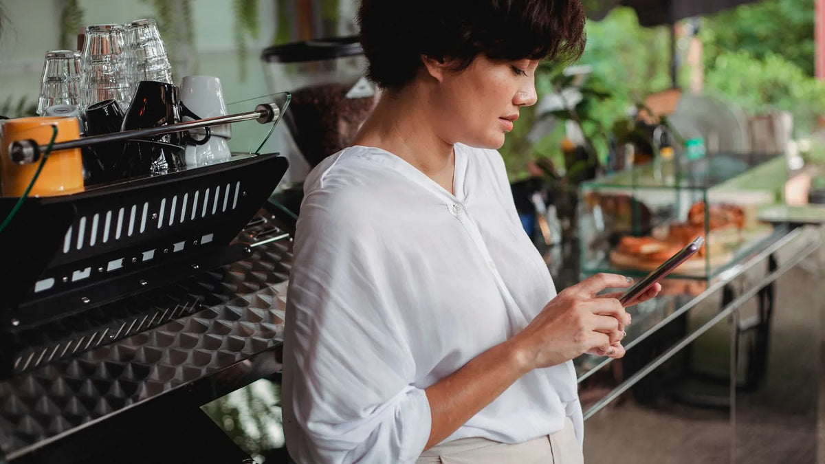 Dueña de una cafetería revisando su celular detrás del mostrador