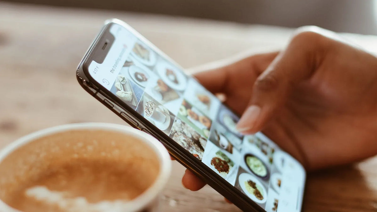 Mano desplazando un feed de fotos en el celular junto a una taza de café