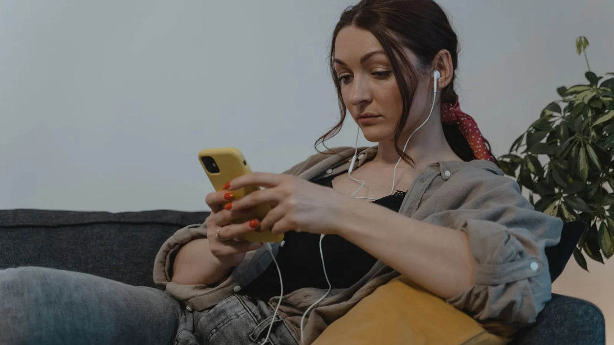 Mujer mirando un video en su celular con audífonos en un sofá