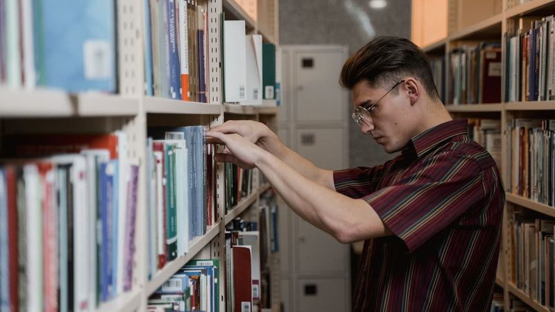 Hombre buscando un libro en los estantes de una biblioteca