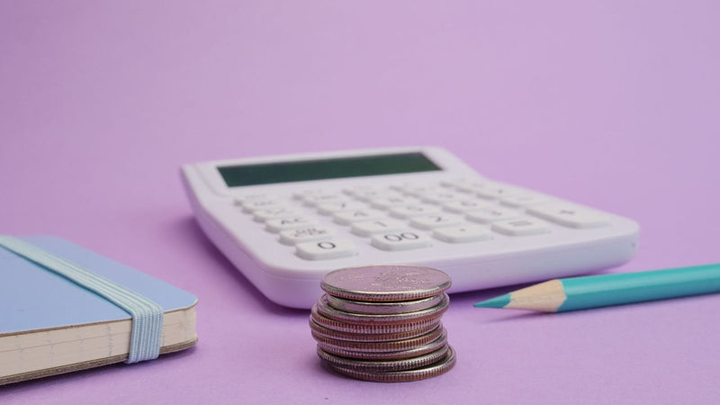 Calculadora, monedas y un lápiz sobre fondo lila