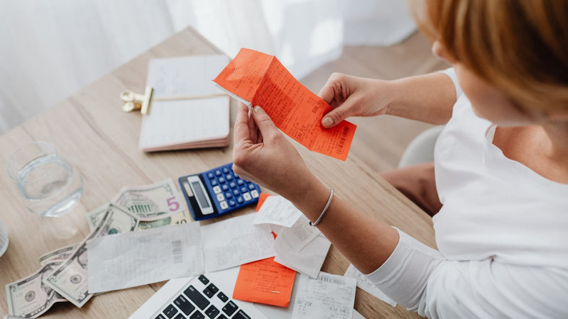 Mujer revisando un recibo naranja junto a una calculadora