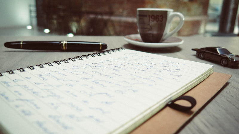 Cuaderno abierto con notas, una pluma y una taza de café