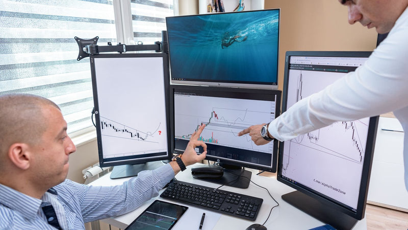 Dos personas revisando gráficos en varios monitores de una oficina