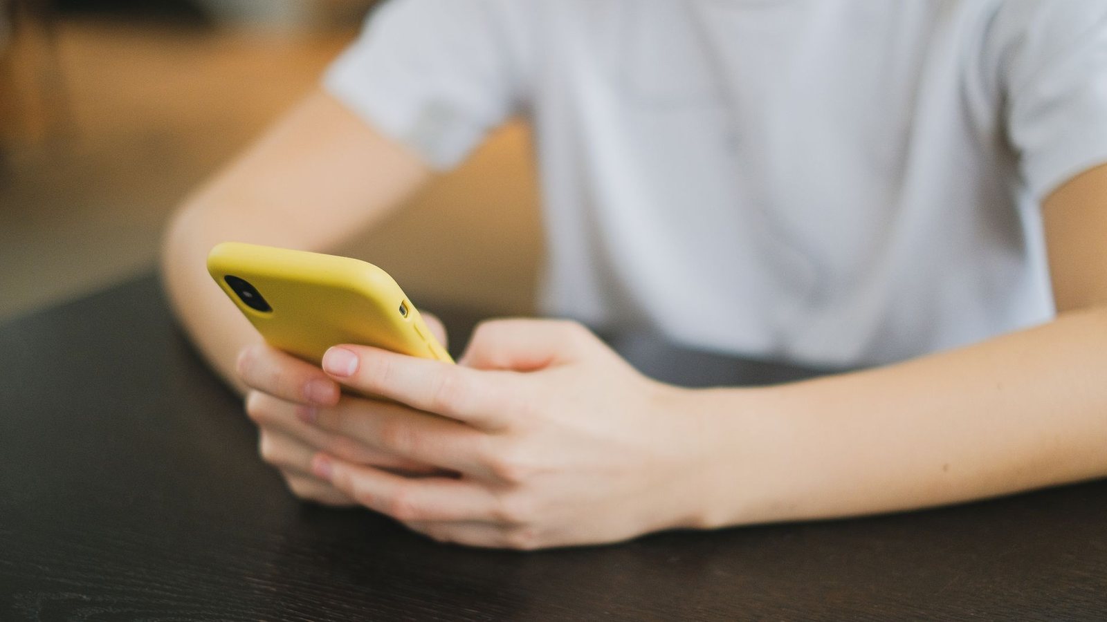Persona sosteniendo un celular amarillo sobre una mesa