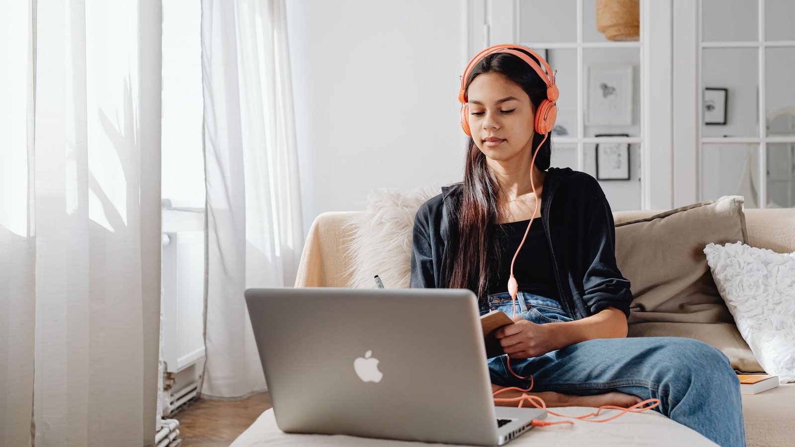 Mujer con audífonos estudiando con su laptop en un sofá