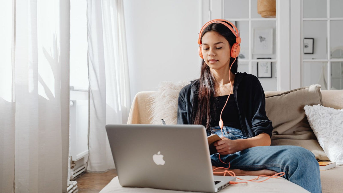 Mujer con audífonos estudiando con su laptop en un sofá
