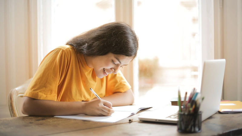 Chica sonriendo mientras estudia y escribe en un cuaderno