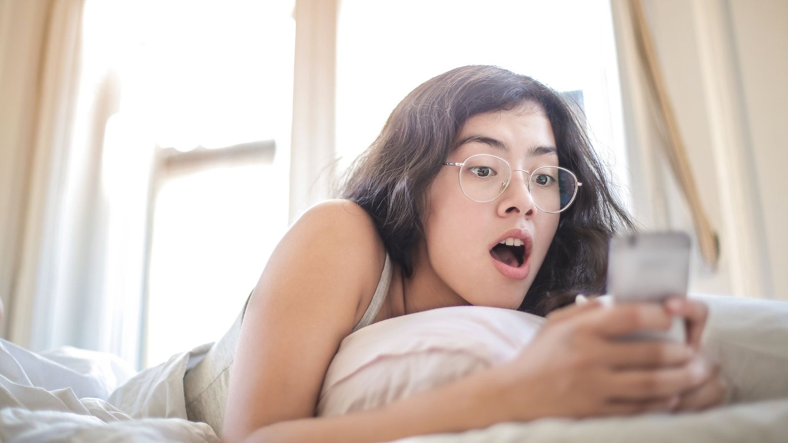Mujer sorprendida mirando su celular en la cama