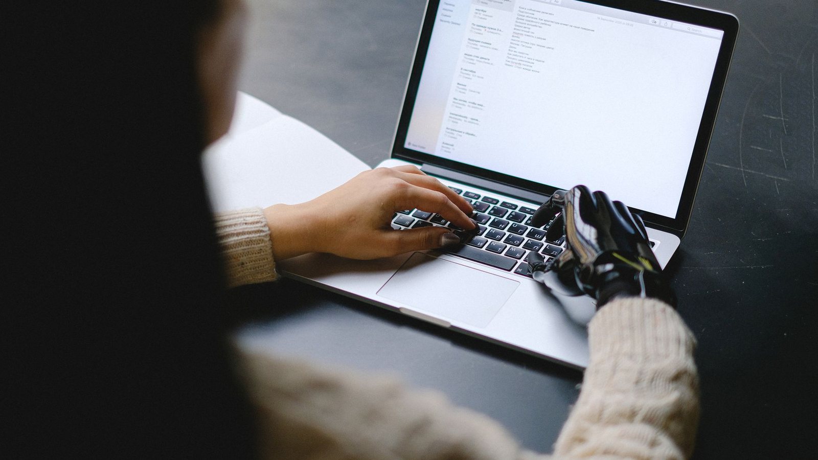 Manos escribiendo en una laptop sobre un escritorio oscuro