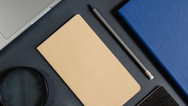 Libretas, bolígrafo y laptop ordenados sobre un escritorio oscuro